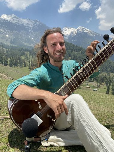 Yoav Fekete (YoYo Sitar) with his sitar and a recording microphone before the snowy mountains of Aru, Kashmir