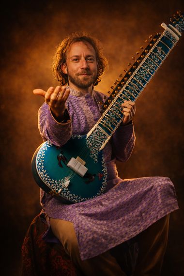 Studio portrait of Yoav Fekete, known as YoYo Sitar, holding his blue sitar