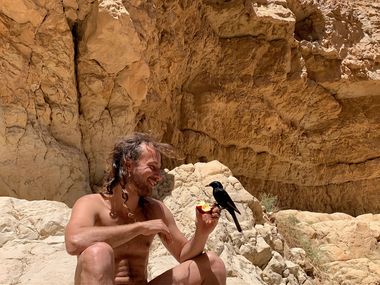 Yoav Fekete (YoYo Sitar) in a desert canyon, offering fruit to a small black bird